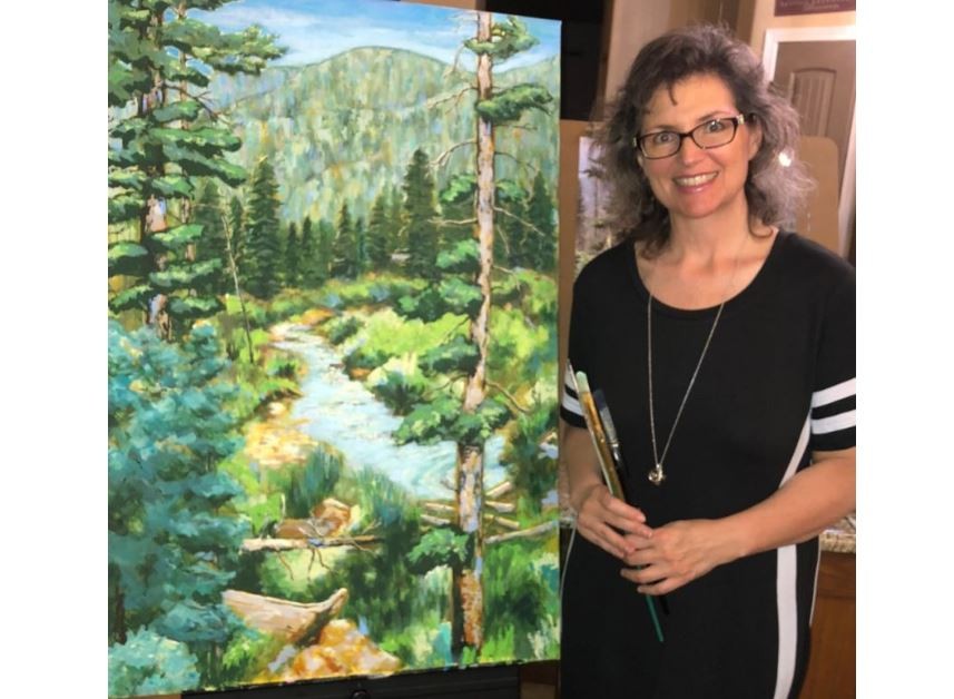 Rhonda stands with paint brushes next to one of her paintings